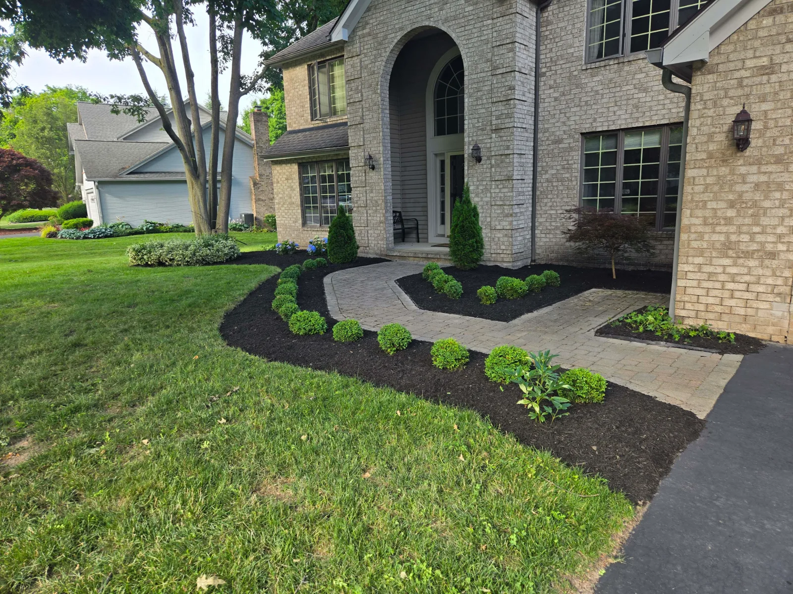 A curved paver walk to the front door of a brick house, between freshly mulched beds of small shrubs