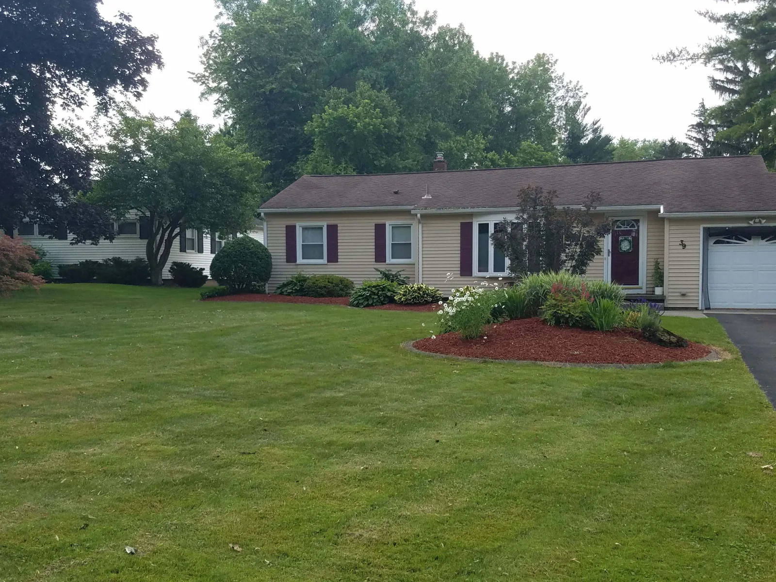 A freshly mowed front lawn and a red-mulched island bed in front of a tan ranch house