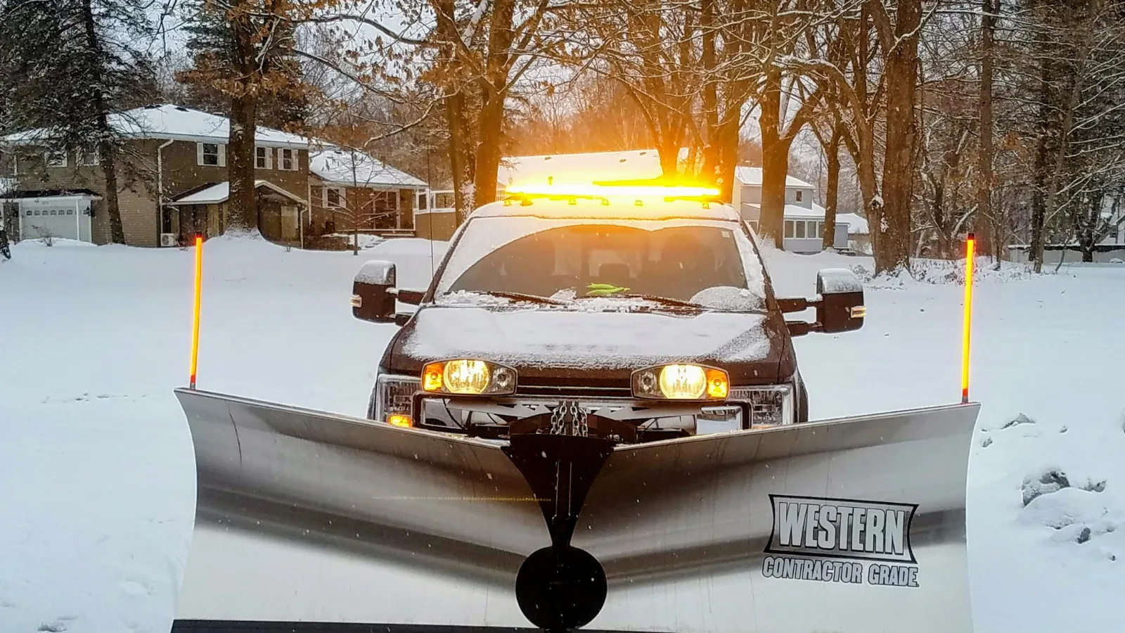 A pickup with a Western plow and an amber light bar in a snowy driveway